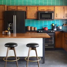 two stools are in front of the kitchen counter and refrigerator with blue tiles on it