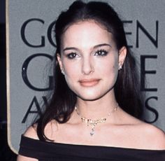 a woman wearing a black off the shoulder dress and gold jewelry with her hair in a pony tail