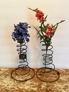 two metal vases with flowers in them on a table