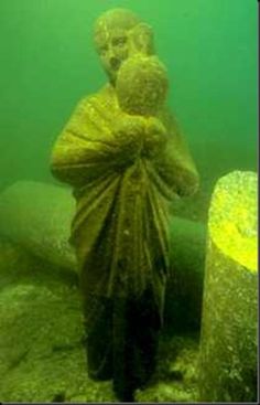 a man is standing in the water next to a large piece of driftwood and looking at something