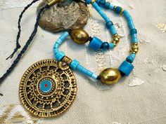 Be unique! Each jewel exists in only one copy and you will be the only one to wear it.  A mid-length necklace, ethnic rustic style: superb pendant of Indian origin! Beautiful and large brass beads that blend perfectly with the blue of the glass beads.  The pendant: 2,4' in diameter in old gold metal and I added a small blue enamel cabochon.  the beads of the necklace:  - large oval brass beads (25 mm)  - large commercial beads in blue opaque glass (15 mm)  - textured blue opaque glass beads (10 Bohemian Blue Jewelry With Gold Beads, Bohemian Brass Necklace For Festivals, Bohemian Brass Necklaces For Festival, Bohemian Brass Jewelry With Round Beads, Bohemian Gold Beads For Festival, Festival Beaded Brass Necklace, Festival Bronze Beaded Necklaces, Bohemian Metal Beaded Necklaces For Festivals, Festival Brass Beaded Necklace