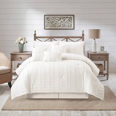 a bed with white comforter and pillows in a room next to a chair, table and lamp