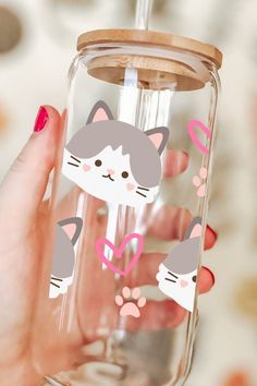 a hand holding a glass with stickers on it and a cat in the bottom