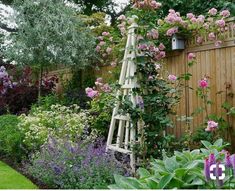 a garden with lots of flowers next to a wooden fence and some plants growing on it