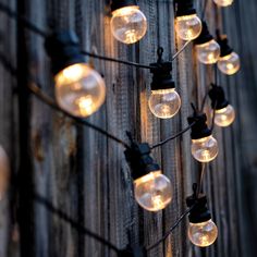 string lights are hanging on the side of a wooden fence with black wire and clear glass globes