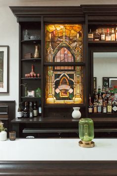 a stained glass window behind a bar with bottles on it and other liquors in the background