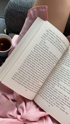 an open book sitting on top of a pink blanket next to a cup of coffee