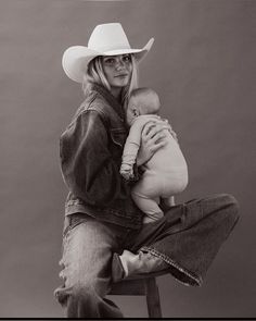 a woman sitting on top of a chair holding a baby wearing a cowboy's hat