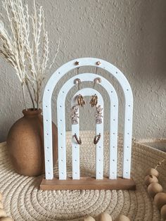 a set of three white wooden earrings stands on a table next to a vase with dried flowers