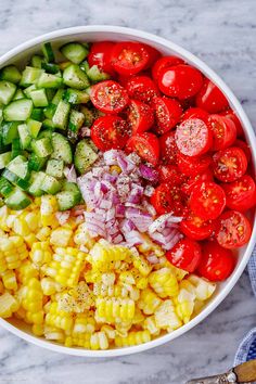 a white bowl filled with corn, cucumber, tomatoes and other vegetables on top of a marble counter