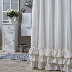 a white shower curtain with ruffles on the bottom and blue rug in front