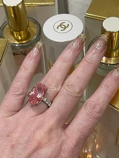 a woman's hand with gold and white nail polish holding a pink diamond ring