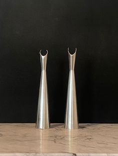 two silver vases sitting on top of a marble countertop next to each other