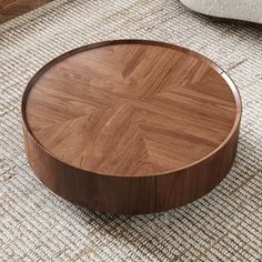 a round wooden table sitting on top of a rug next to a chair and ottoman