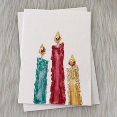 three candles are painted on white paper with gold trim and red, green, blue, and yellow accents