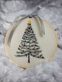 a hand embroidered christmas tree ornament hanging from a hoop on white furnishing