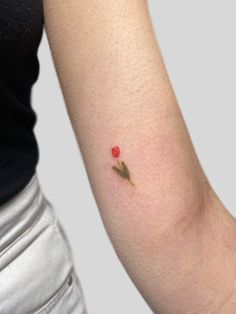 a woman's arm with a small red rose tattoo on the left inner arm