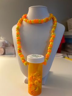 an orange and yellow beaded necklace next to a plastic bottle on a white mannequin