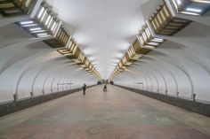 two people are standing in the middle of a long hallway with lights on either side