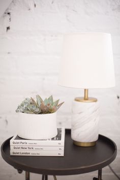 a small table with a lamp and some books on it next to a white brick wall