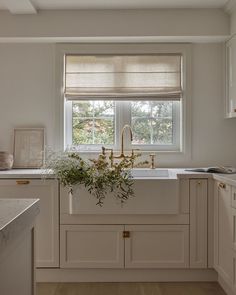 a kitchen with white cabinets and a window above the sink is decorated with greenery