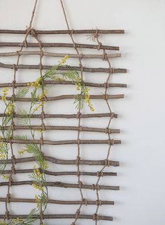 a wall hanging made out of branches and twigs with flowers on it, along with a vase filled with yellow flowers