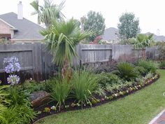 a backyard garden with lots of plants and flowers in the grass, along side a fence