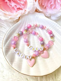 a pink and white bracelet with two hearts on it next to peonie flowers