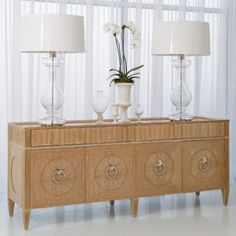 a wooden cabinet with two lamps on top and flowers in vases next to it