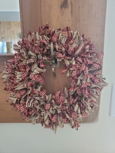 a red and white wreath hanging from the side of a wooden door with burlocks on it