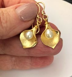 Shop Calla Lily Earrings Gold. Real pearl earrings will add a perfect touch of flair to your outfit!  You can wear it with your evening dress or favorite jeans.  These flower earrings are made from: -Gold plated calla lily flowers (18mm x 13mm)  -White freshwater pearls -Gold filled ear wires Pearl drop dangle earrings are 1.25" long.  It will make a great bridesmaid gift or flower girl gift.  Back to my shop: https://www.etsy.com/shop/jewelrybyirina Your order of bohemian jewelry will be mailed within 2 business days via USPS. US orders and most international orders will have a tracking#. Thank you for visiting Gold Bridesmaid Earrings, Lily Earrings, Calla Lily Flowers, Real Pearl Earrings, Bridesmaid Earrings Gold, Lily Flowers, Flower Girl Gifts, Jewelry Birthday, White Freshwater Pearl