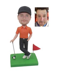 a bobble head golf player with an orange shirt and black cap, holding a red flag