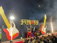 a group of people standing on top of a stage with guitars and fireworks in the air