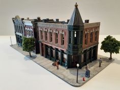 a miniature model of a building with people walking around the front yard and trees on the other side