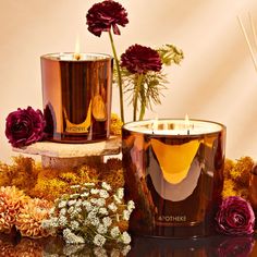 two candles are sitting next to flowers and other items on a table with gold foil