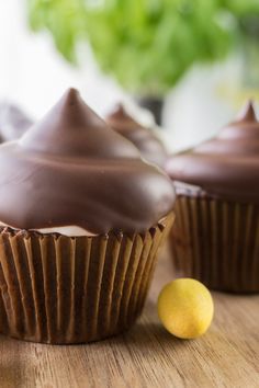 two chocolate cupcakes with frosting and a lemon next to them on a wooden table