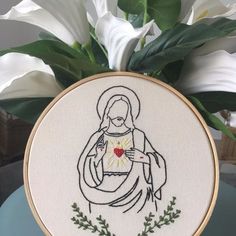 a cross stitched image of the virgin mary holding a heart surrounded by greenery