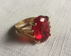 Elegant solitaire red ring set in a gold setting. The gemstone measures .75" by .5"  and it's set in a 18 Kt Electroplated Gold setting. (It says 18 Kt GE inside.) Size 5.75 or maybe 6. Please know that if you don't like the way the ring fits, you can return it; you pay for the shipping, but there's no restocking fee or questions asked, I just refund the ring's cost to you. Please take a look at my storefront at: https://www.etsy.com/shop/FabFinds42?ref=seller-platform-mcnav I have a wide select Red Gem Ring, Gold Ring Big, Red Ring, Red Rings, Red Jewel, Costume Rings, Chunky Ring, Jewels Rings, Chunky Jewelry