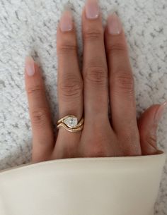 a woman's hand wearing a gold ring with a diamond in the middle, on top of a white cloth