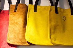 four different colored bags hanging from hooks on a white wall with black handles and leather handles