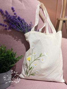 a white tote bag with daisies on it next to a potted plant