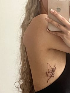 a woman with a small tattoo on her arm holding a cell phone and taking a selfie