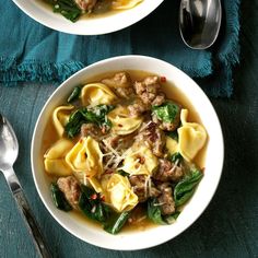 two white bowls filled with pasta and spinach on top of a blue table cloth