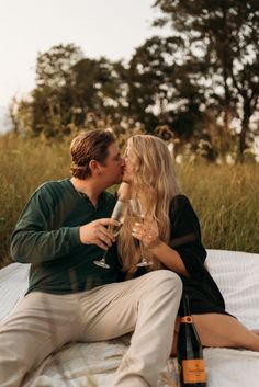 a man and woman sitting on top of a bed kissing while holding glasses of wine