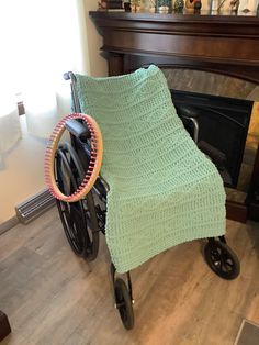 a green crocheted blanket sitting on top of a wheel chair next to a fireplace