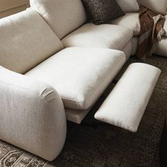 a white couch with pillows on top of it in front of a chair and ottoman