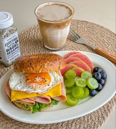 a breakfast sandwich with eggs, ham, cheese and fruit on a plate next to a cup of coffee