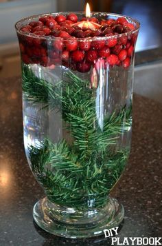 a candle that is inside of a glass vase filled with berries and greenery on a table