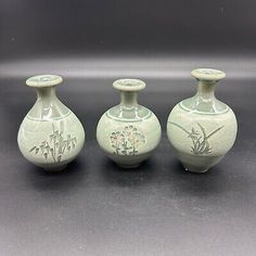 three green vases sitting next to each other on a gray surface with white flowers