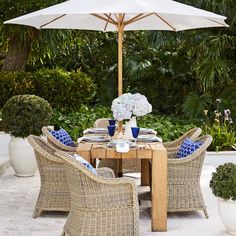 an outdoor table with chairs, umbrella and potted plants